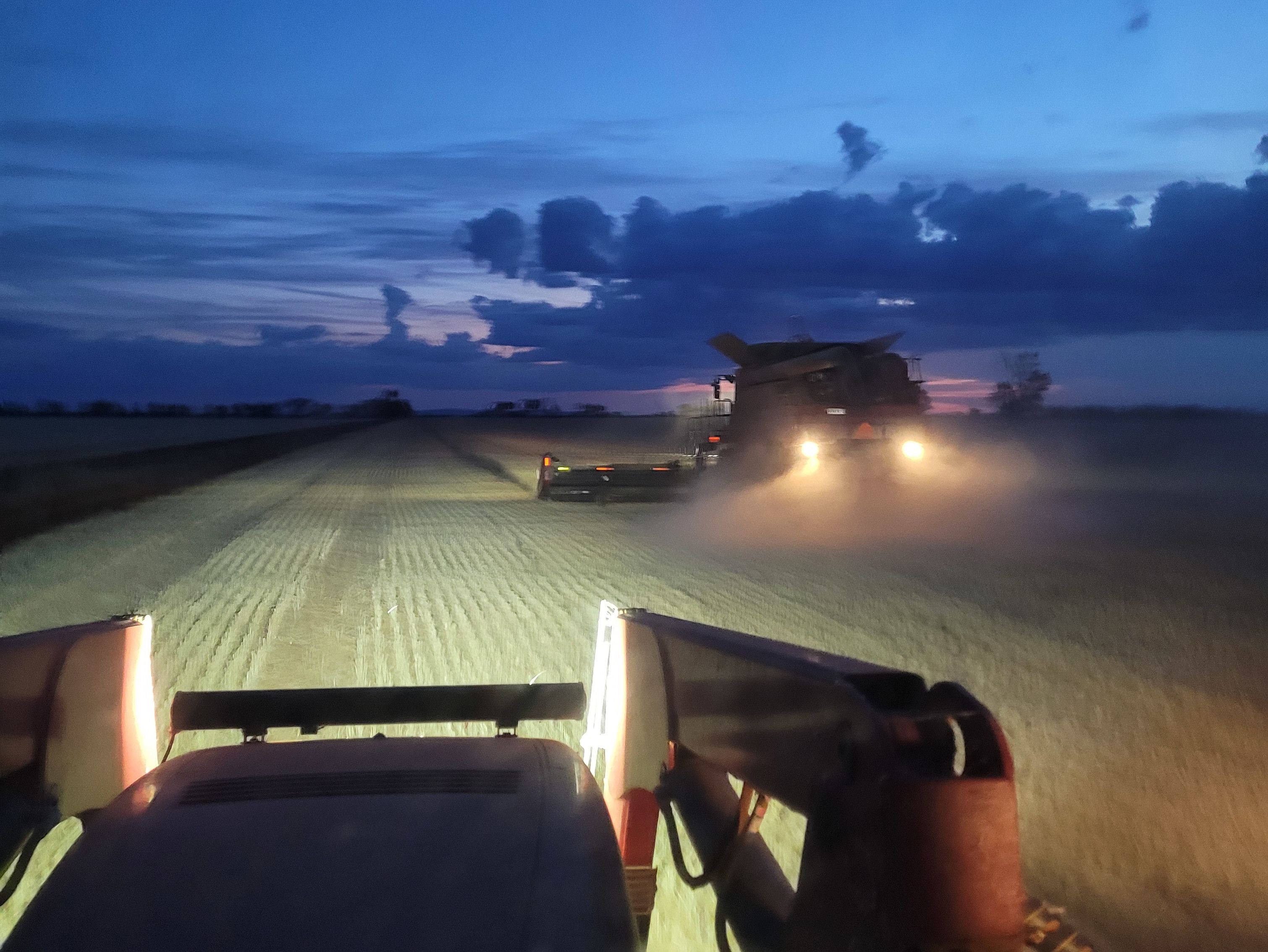 View from inside a tractor in a field behind a harvester at dusk