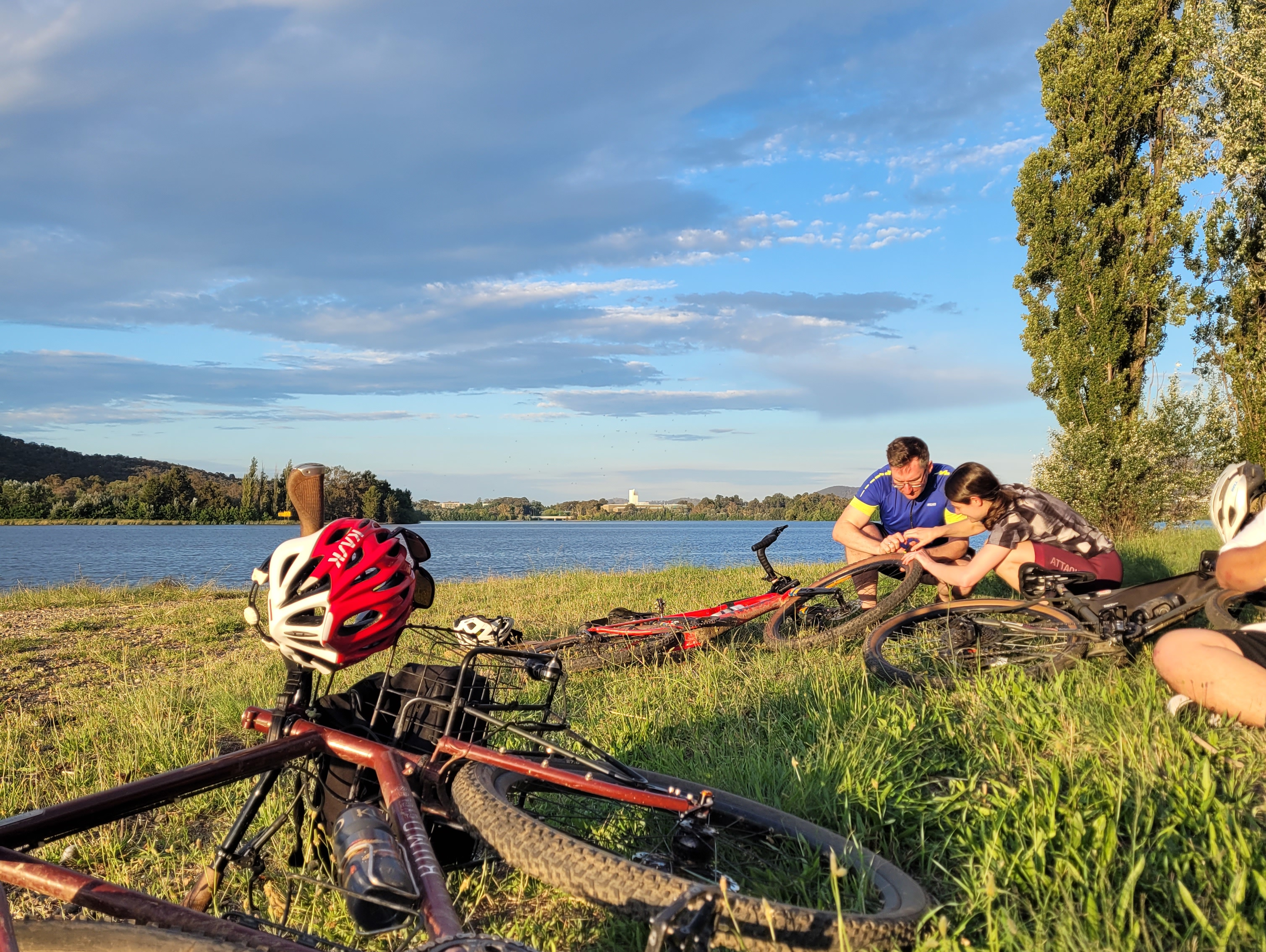 Collection of bikes on a lake shore with two people working on a bike