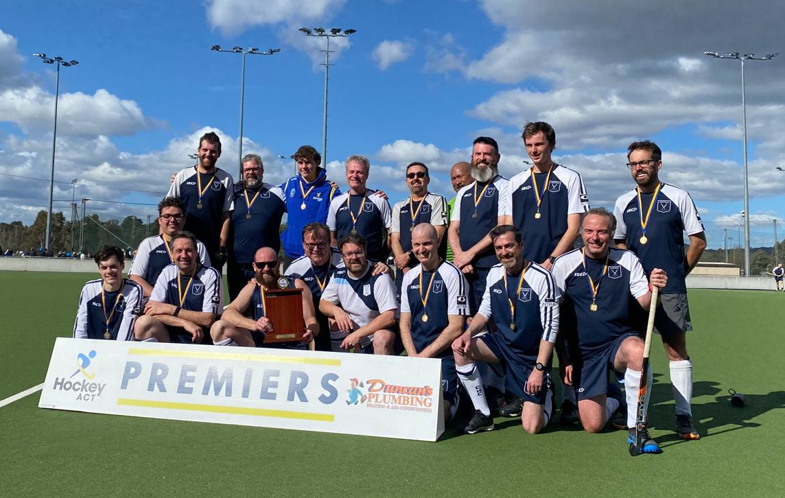 Group of men on a hockey field standing around a 2024 Premiers sign