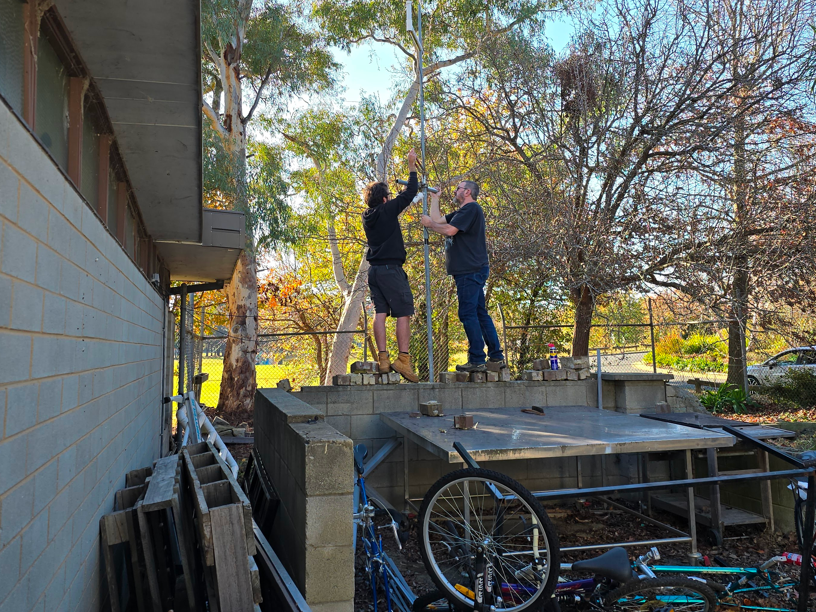 Two men standing on a wall mounting an antenna
